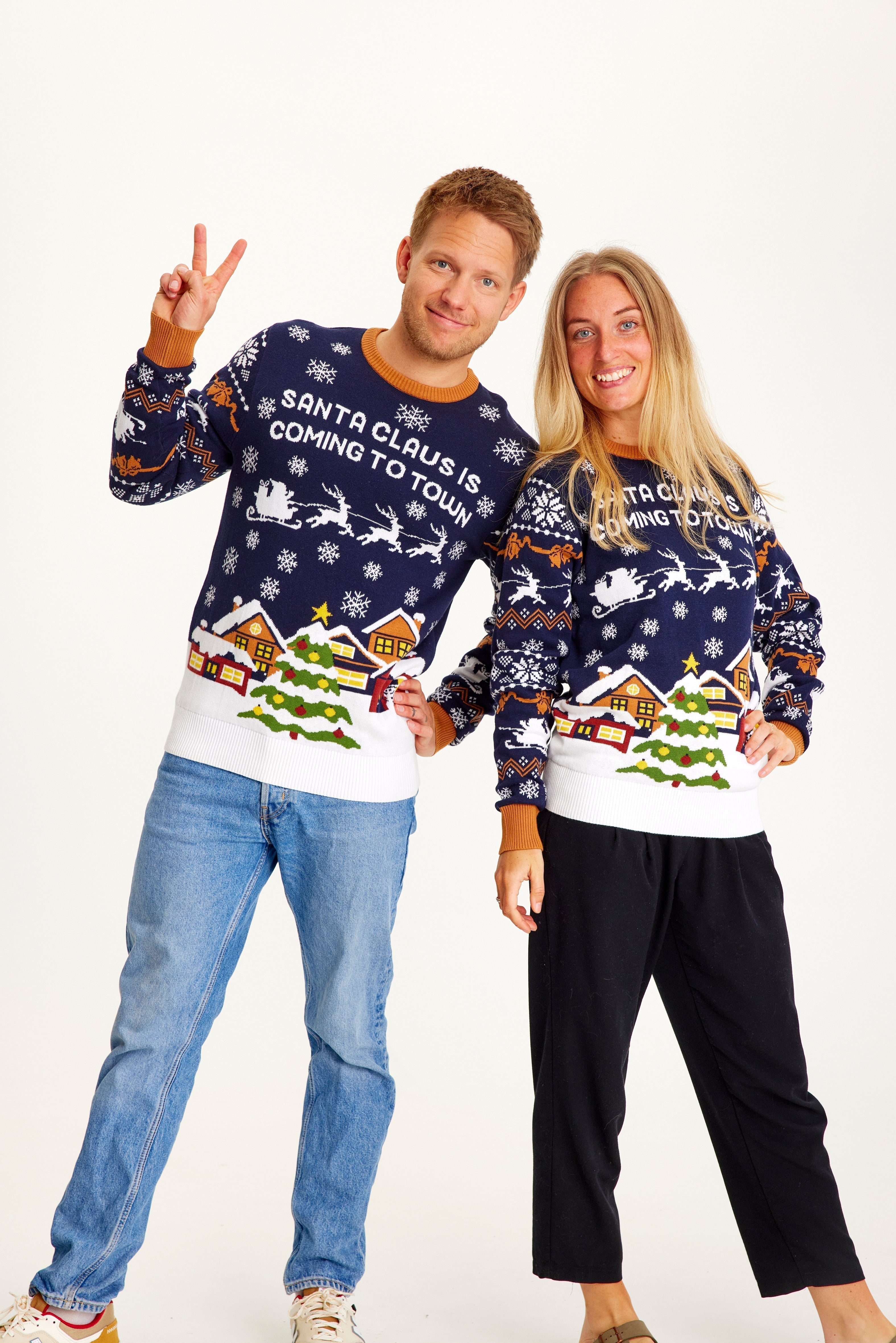 Un couple posant avec un pull de Noël bleu foncé et blanc orné d'un sapin de Noël.