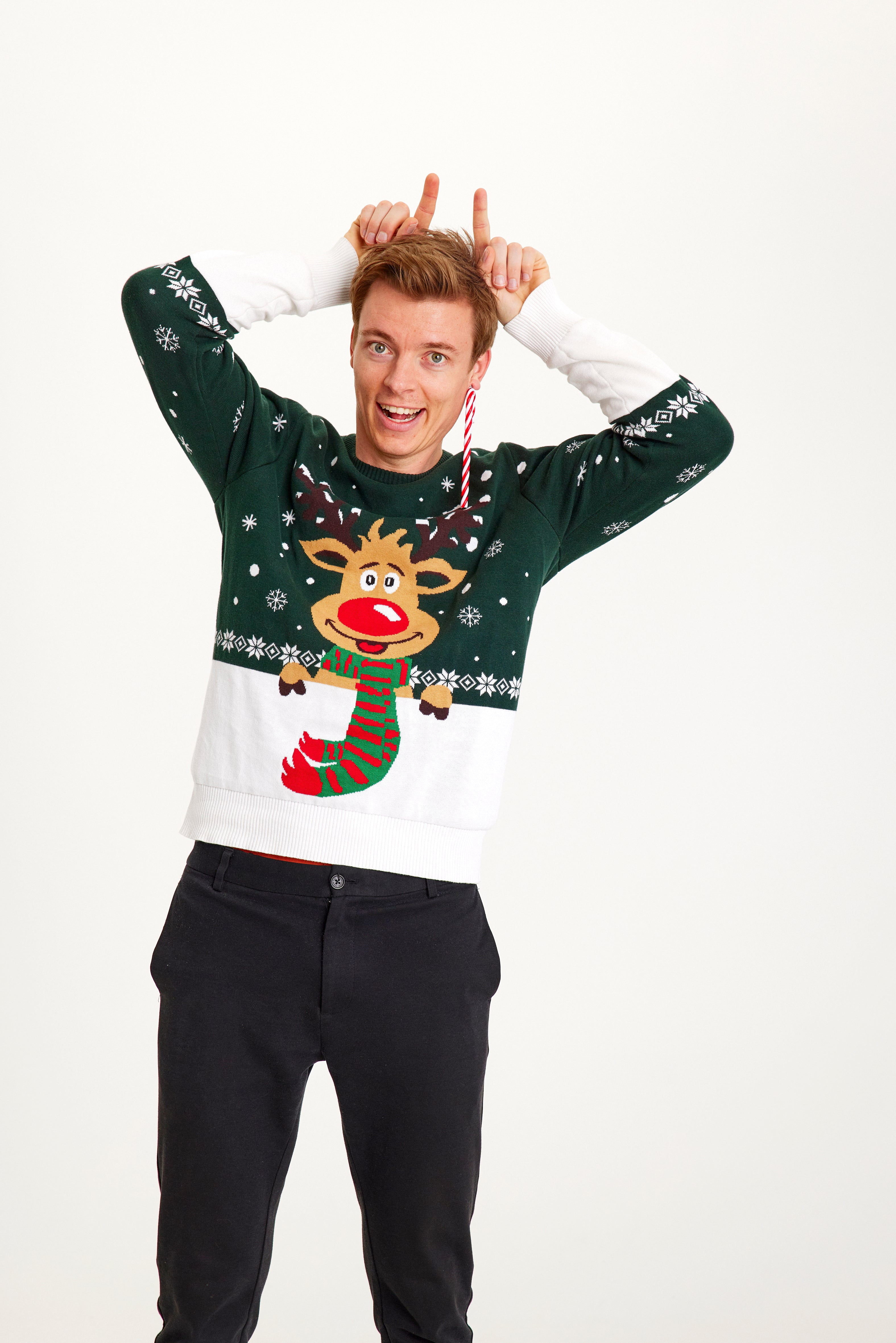 Un homme posant avec un pull de Noël vert et blanc orné de Rudolph.