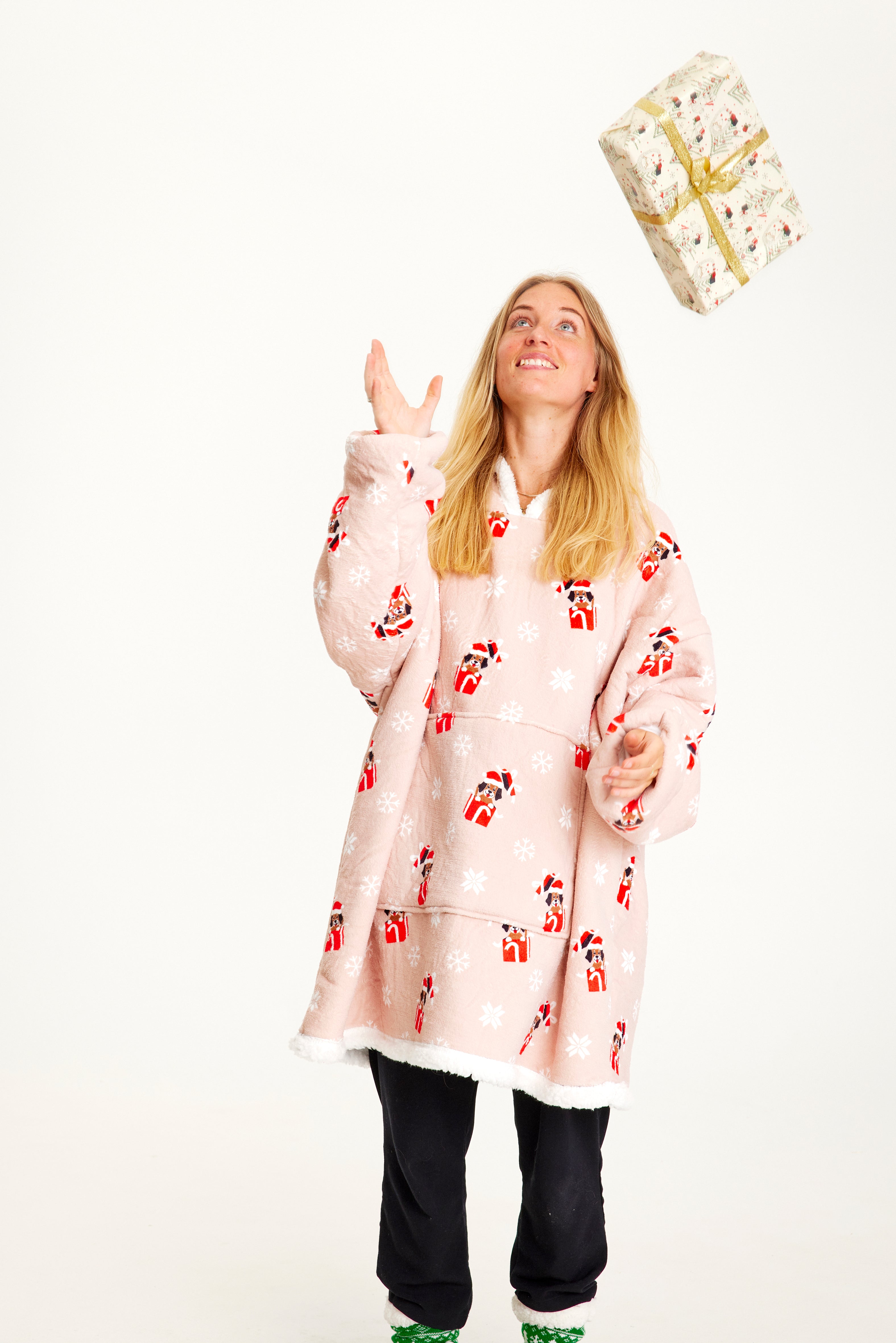 Une femme avec un cadeau de Noël portant un sweat à capuche de Noël rose avec des chiens dessus.