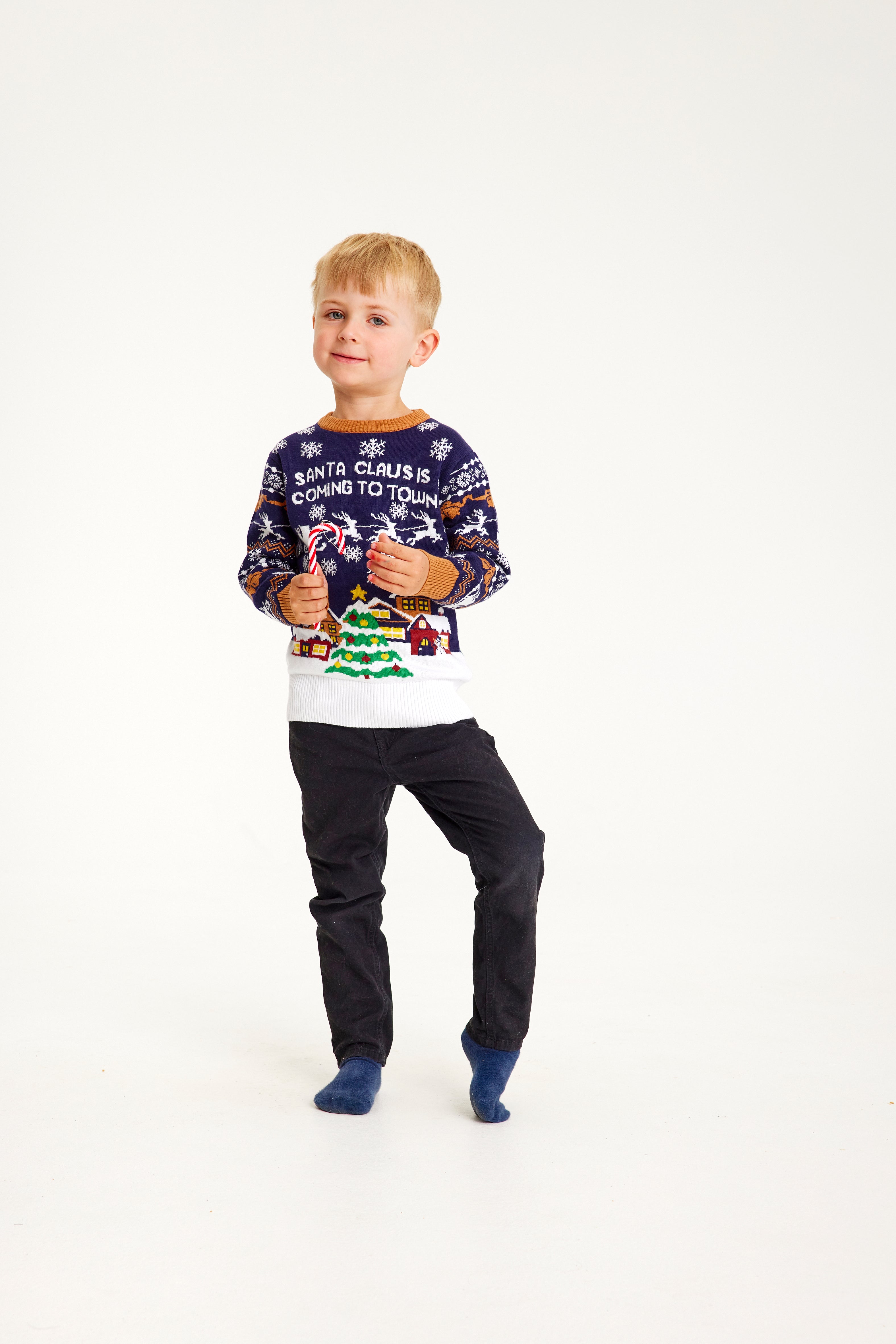 Un enfant posant avec un pull de Noël bleu foncé et blanc orné d'un arbre de Noël.
