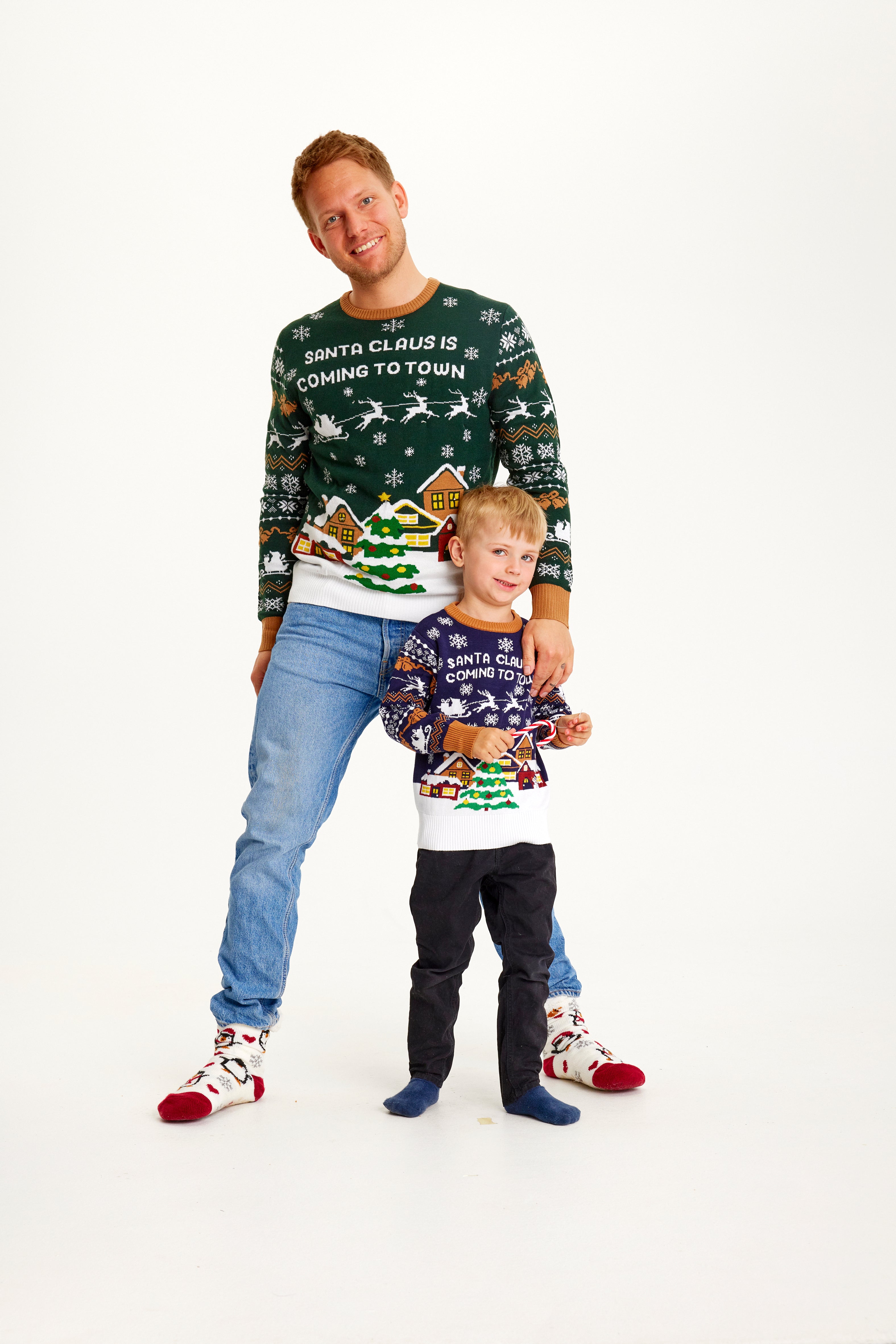 Un homme et un enfant posant ensemble vêtus d'un pull de Noël orné d'un arbre de Noël.