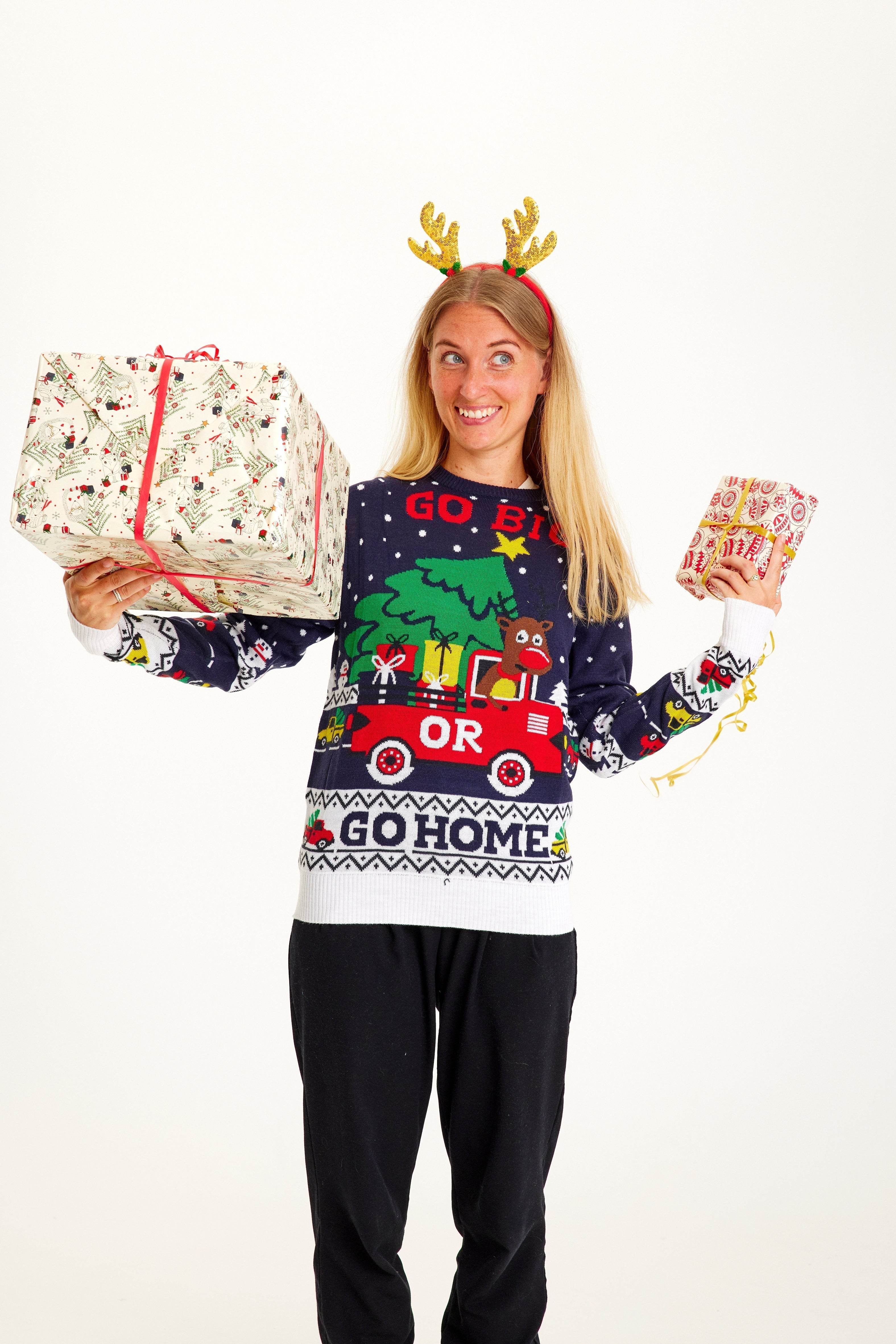 Une femme avec des cadeaux de Noël dans les mains, portant un pull de Noël avec la citation 