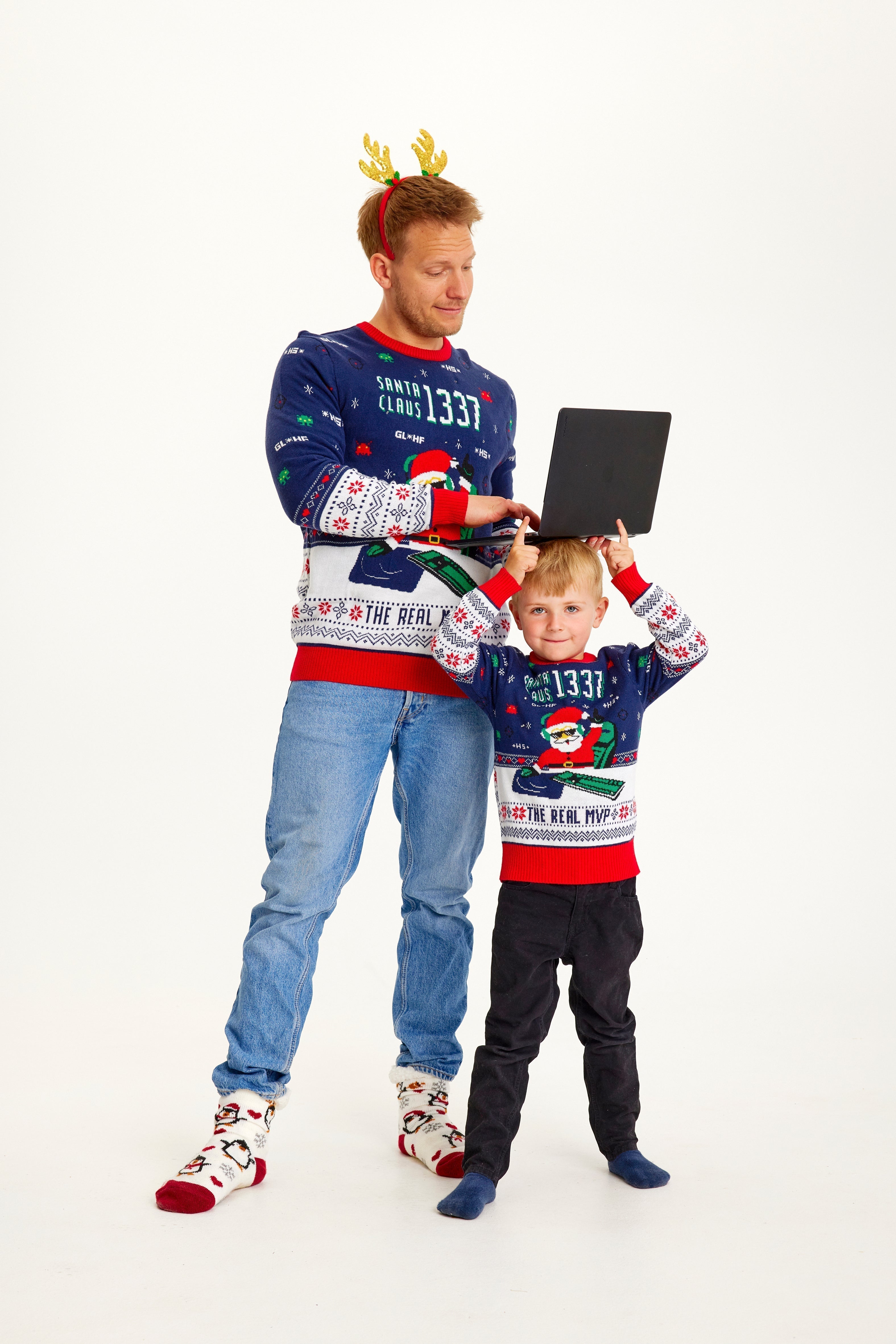 Un enfant et un homme portant un pull de Noël bleu et rouge avec un Père Noël et des lumières.
