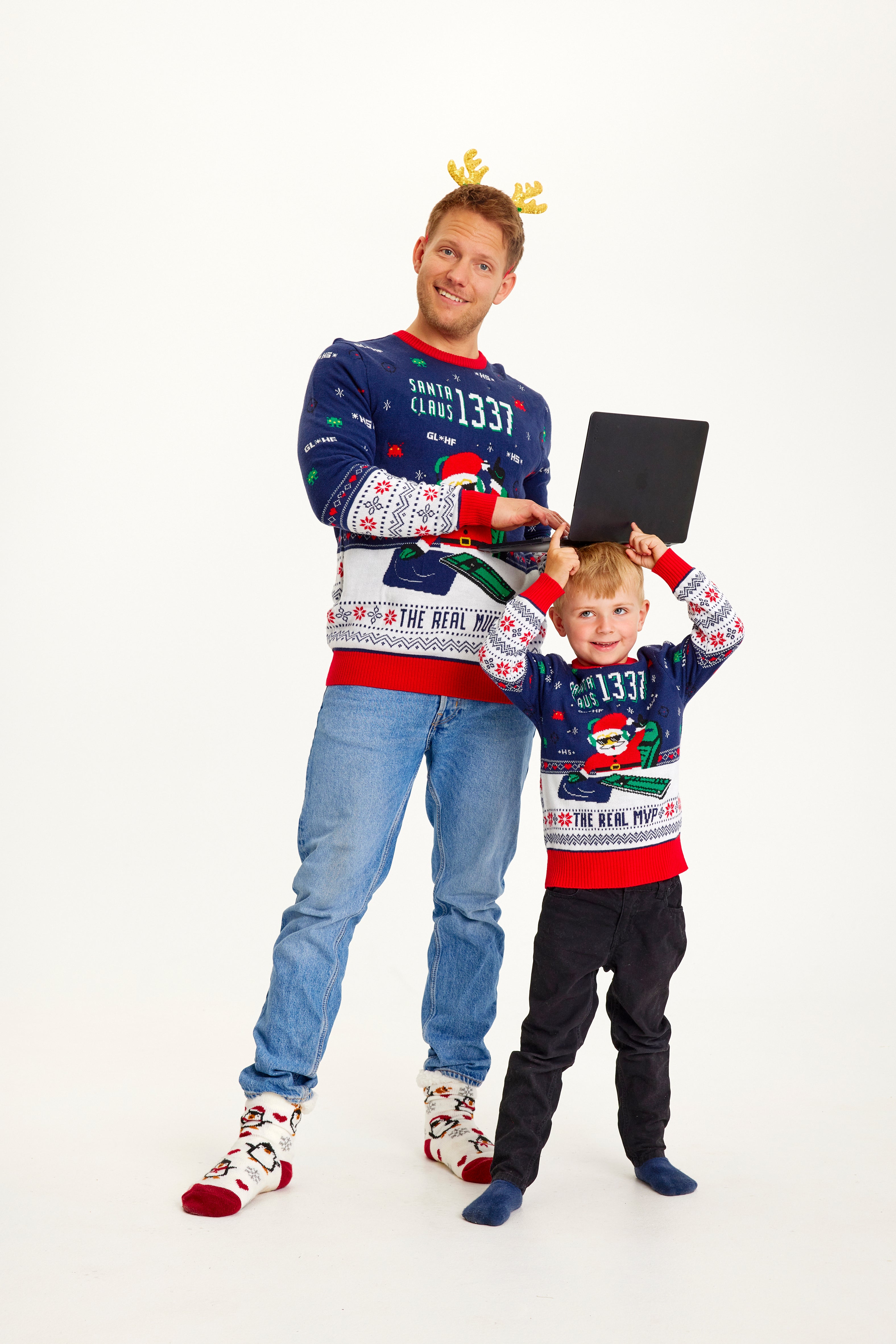 Un homme et un enfant portant un pull de Noël bleu et rouge avec un Père Noël et des lumières.